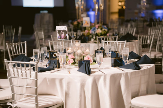 Event table with white tablecloth, silver chairs, and floral centerpiece.