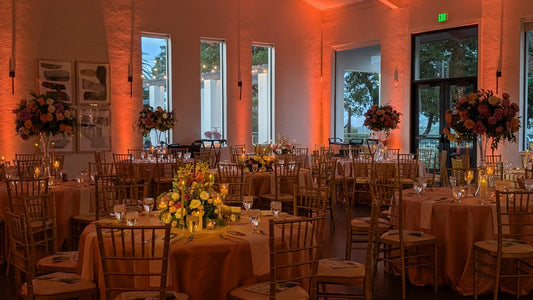 Elegant event room with floral centerpieces and warm orange lighting.